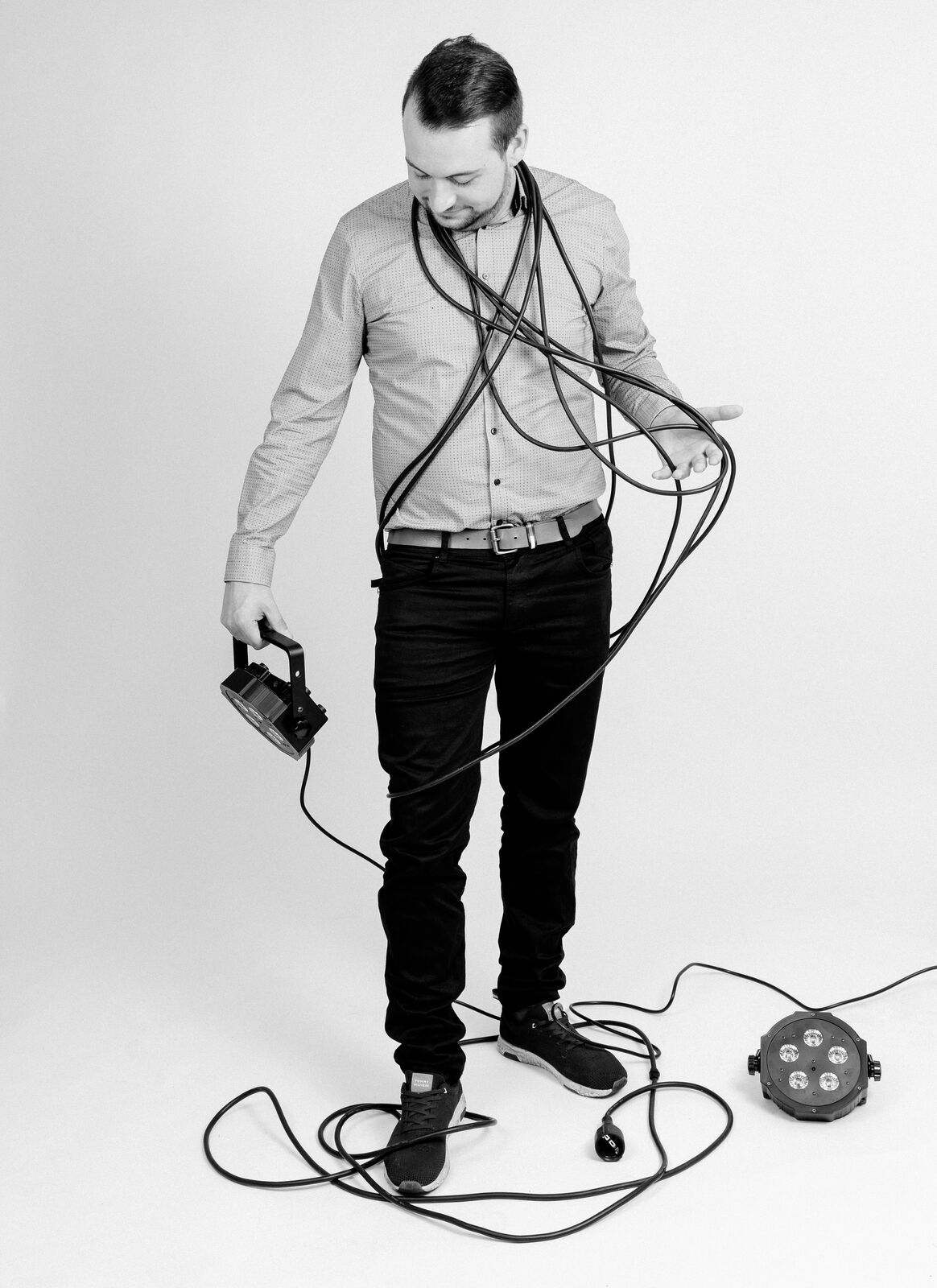 Oliver Groß steht mit Kabeln und einem LED-Scheinwerfer in der Hand vor einer hellen Wand