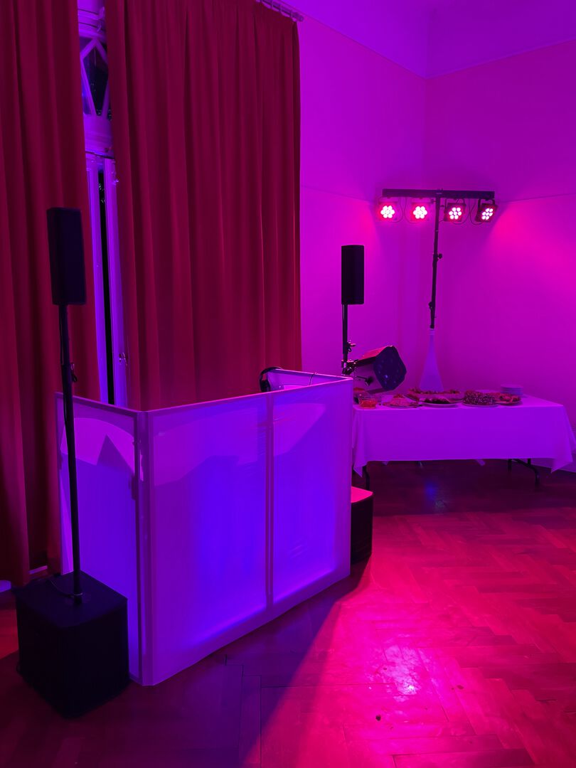 Saal mit lila Licht an den Wänden und DJ-Pult