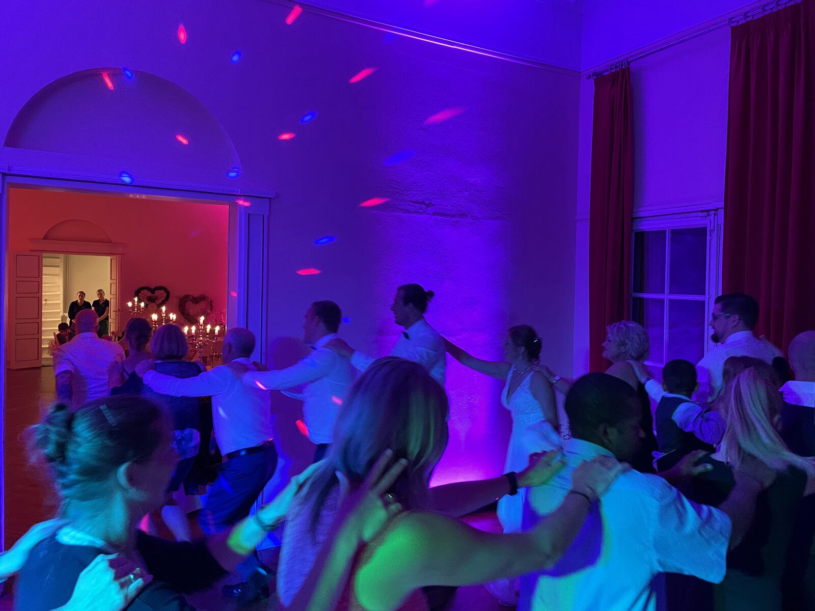 Volle Tanzfläche in einem Saal, bunt angestrahlt