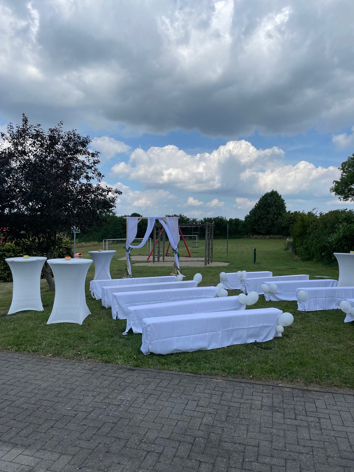 Stuhlreihen mit weißen Hussen und Stehtische für eine Trauung im Garten